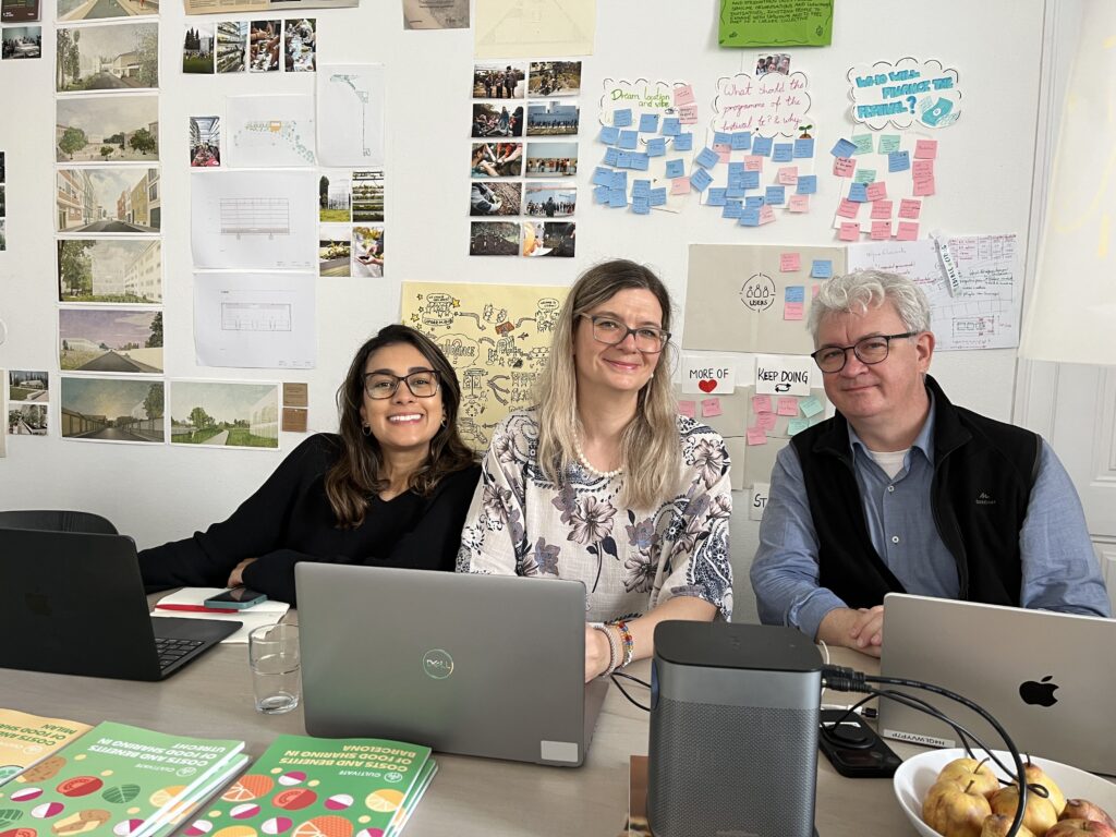 Three people sitting around a desk in a collaborative workspace, surrounded by walls covered with colourful sticky notes